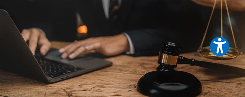 Lawyer typing on laptop beside gavel and scales of justice, symbolizing legal work and accessibility.