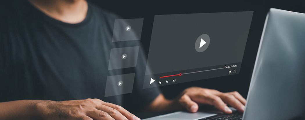 A person using a laptop with floating video player icons on the screen, representing online media streaming or video content interaction.
