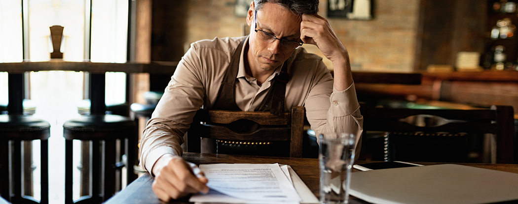 Small business owner looking worried while reviewing lawsuit documents in a restaurant setting.
