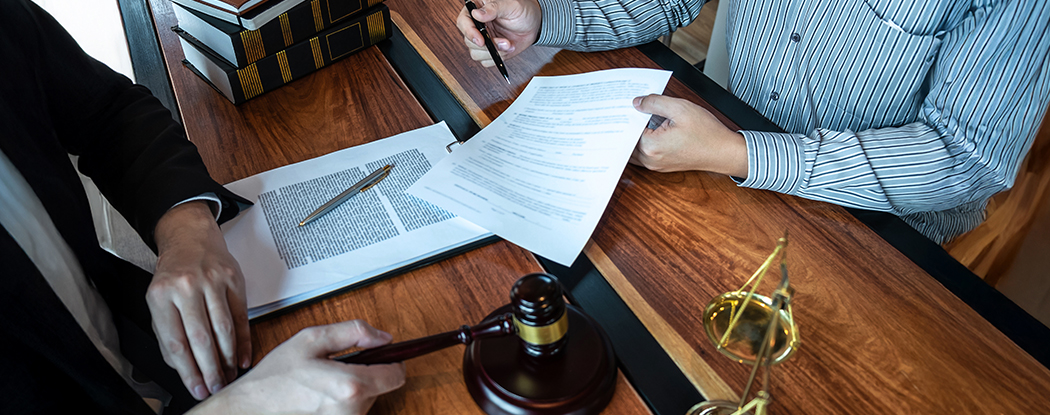 Two people reviewing legal documents at a desk with a gavel, scales, and books.