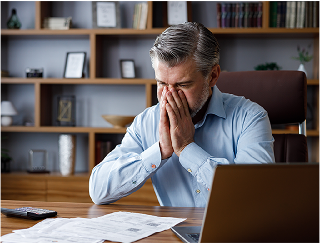 A stressed man sits at a desk with Accessibility Lawsuit documents, holding his face while looking at a laptop and Accessibility Lawsuit documents