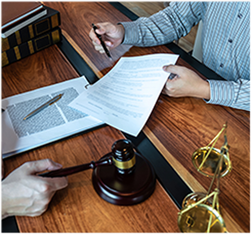 Two people reviewing legal documents at a desk with a gavel, scales, and books.